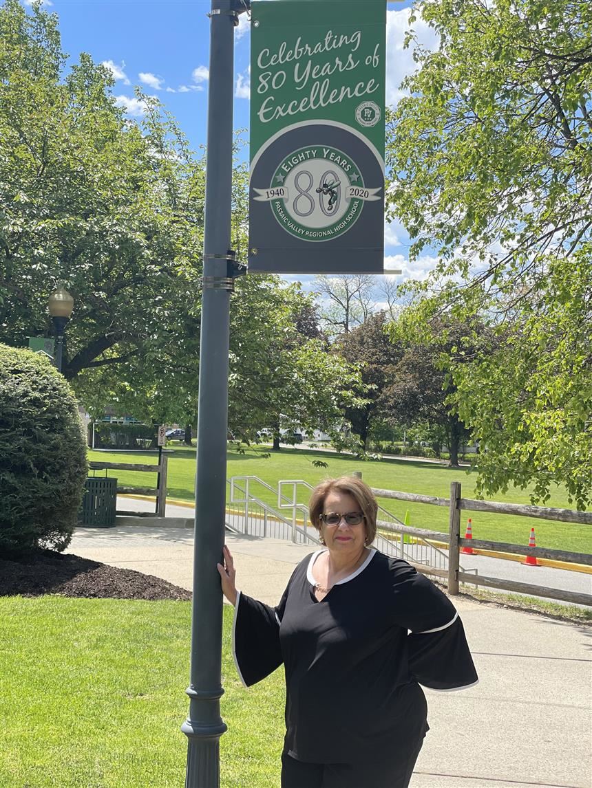 Dr. Cardillo standing under an 80th Anniversary of PV flag; photo credit: Rae Allex
