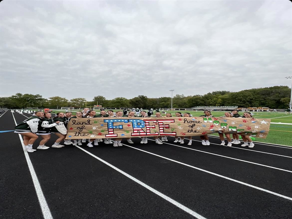 Cheerleaders pose with banner before Homecoming football game